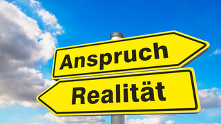 dieses Foto zeigt zwei Straßenschilder mit der Aufschrift "Anspruch" und "Realität"